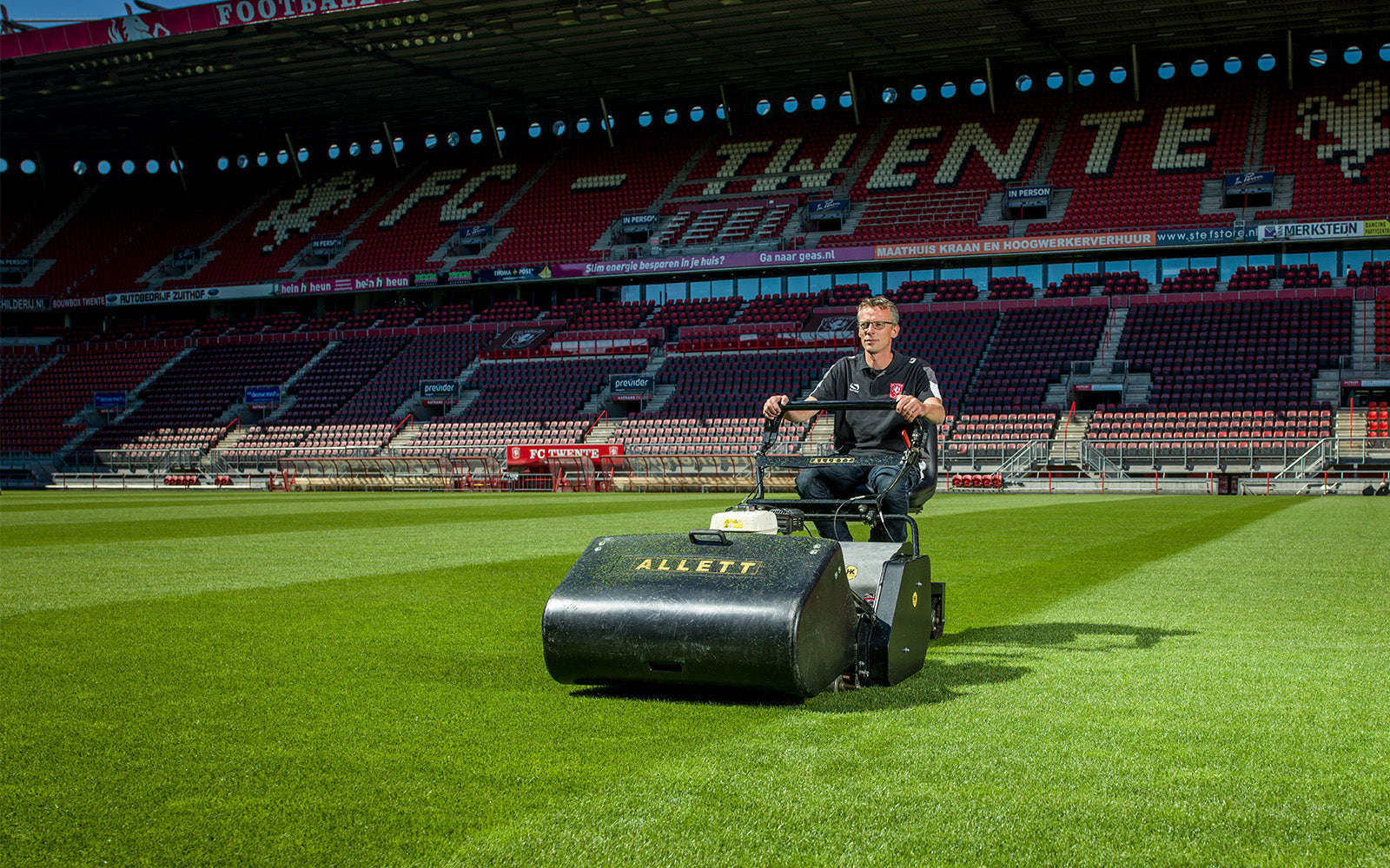 Groundsperson using an Allett professional cylinder mower on a striped football pitch at FC Twente stadium.